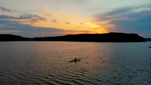 Aerial shot flying over a silhouette kayaker in archipelago water toward a colorful sunset in background
