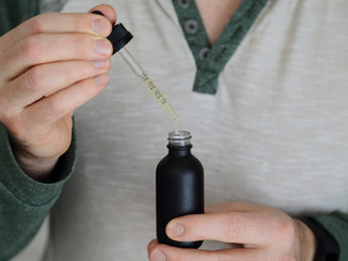 A bottle and dropper of CBD and THC tincture solution is shown up close, being held by a pair of male hands.