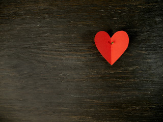One red paper heart is nailed on a black old wooden background
