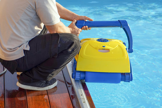 A pool cleaner holds a robot cleaner. Pool cleaner during his work. Caucasian hotel staff worker cleaning the pool.