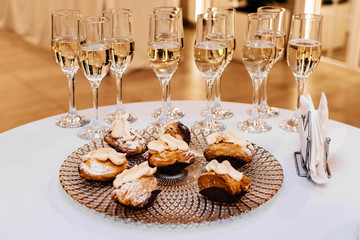 Champagne in glasses and a plate with cakes on the white table