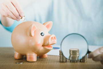 Female hand putting euro coin into a piggy bank. Coin tower growth under the magnifying glass....