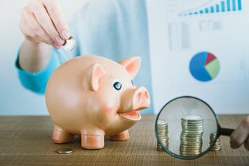 Female hand putting euro coin into a piggy bank. Coin tower growth under the magnifying glass....