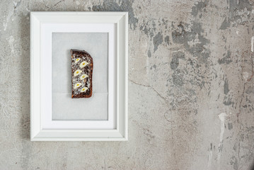 Concept of food. Black bread sandwich with butter, salt and slices of garlic in a white picture frame on a concrete gray wall. Creative poster