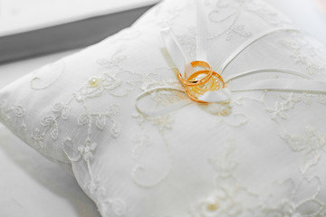 gold wedding rings on a white cushion with pearls