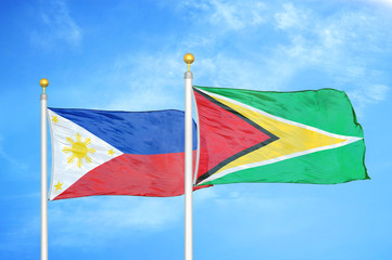 Philippines and Guyana two flags on flagpoles and blue cloudy sky