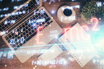 Physics and math theme hologram with formula drawings over computer on the desktop background. Top...