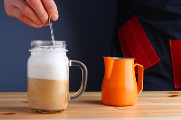 milk shake with coffee on wooden table and grey background. coffee shake with pitcher and barista hand