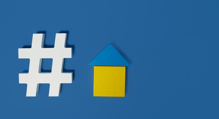 Stay home concept. Hashtag symbol and figurine of a wooden house on a blue background. Empty area for text.