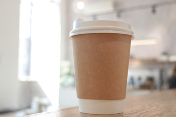 Mock up with a cup of coffee. A glass is on the table in a cafe, selling coffee in the background. Coffee to go. Light walls. Wooden table. Cafe. Disposable cup