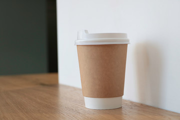 Mock up with a cup of coffee. A glass is on the table in a cafe, selling coffee in the background. Coffee to go. Light walls. Wooden table. Cafe. Disposable cup