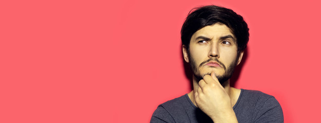 Studio portrait of young thoughtful and confident guy on background of pastel coral pink color with copy space.