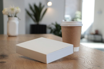 On the table is a mockup of a coffee cup and a white book. white box suitable for layout. Empty white background for design. White notebook. without text. Layout for overlaying your brand. Coffee 