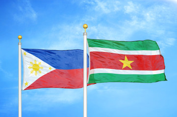 Philippines and Suriname two flags on flagpoles and blue cloudy sky