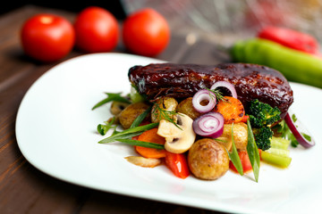 A calf steak with a young potato and juicy vegetables on a wooden background