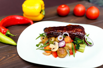 A calf steak with a young potato and juicy vegetables on a wooden background