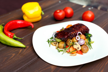 A calf steak with a young potato and juicy vegetables on a wooden background