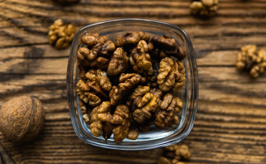 Walnut in a smale plate with scattered shelled nuts and whole nut which standing on a wooden vintage table. Walnuts is a healthy vegetarian protein nutritious food. Walnut on rustic old wood.