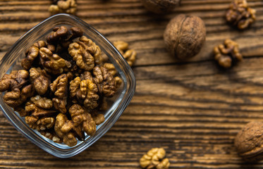 Walnut in a smale plate with scattered shelled nuts and whole nut which standing on a wooden vintage table. Walnuts is a healthy vegetarian protein nutritious food. Walnut on rustic old wood.