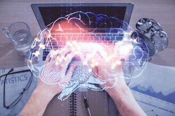 Double exposure of man's hands typing over computer keyboard and brain hologram drawing. Top view....