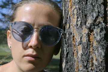 Portrait of a girl with closed eyes in blue glasses, leaning her head against a tree. The concept of communication with nature, love and care for the planet. Meditation, close-up