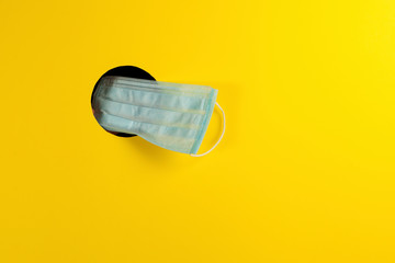 Disposable medical face mask through a hole in a yellow background. Place for text