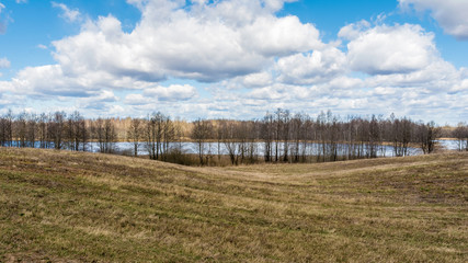 Landscape of European plains with hills and lowlands, lake, meadows and forests. Blue sky with clouds over horizon.