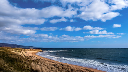 Brora beach in the Highlands of Scotland washed by surf at high tide on a sunny day with blue skies and white clouds