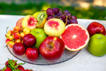 a glass plate with peaches, cherries, grapefruit, apples, pears and kiwi on tablecloths