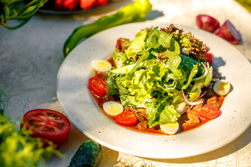 salad with fresh vegetables and meat, with lettuce, yatsami, tomatoes on a white plate