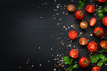 Fresh cherry tomatoes, parsley, sea salt, black and pink pepper, on black slate stone background. Top view.