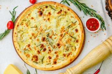 hot pizza with onions and basil on a wooden surface with vegetables on a white table