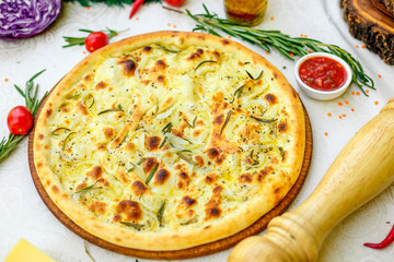 hot pizza with onions and basil on a wooden surface with vegetables on a white table