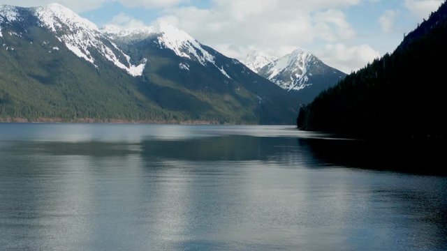Chilliwack Lake with dead fallen tree trunks and driftwood in the foreground and the reflecting Mount Redoubt (Skagit Range Mountains) in the background.