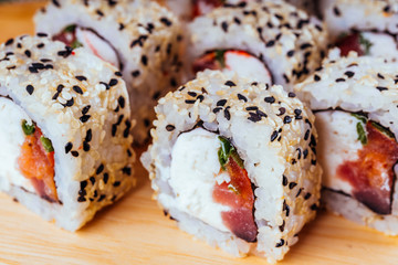 Delicious rolls on wooden board on decorative bamboo napkin. Close up of tasty sushi rolls on cutting board.