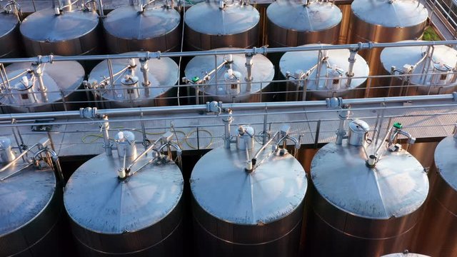 Oil barrels in a factory. Rows of tall stainless steel tanks connected with pipes. Shiny silos in a chemical industry plant. Metal containers with hazardous chemicals. Aerial footage.