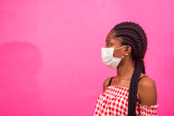 closeup of a beautiful african lady wearing face mask isolated over pink background preventing,...