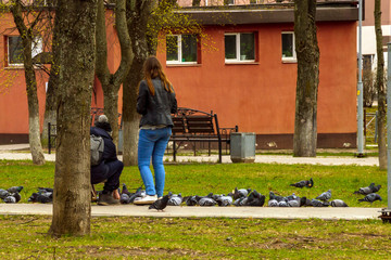 A girl and a young man in a city park feed pigeons.