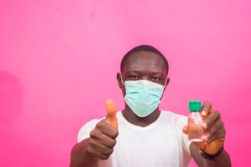 young african man wearing face mask preventing himself from the outbreak in the society holding a hand sanitizer, sterilizer and did thumbs up