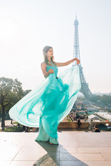 Naklejka premium Beautiful girl in an azure evening dress in Paris with the Eiffel tower in the background.