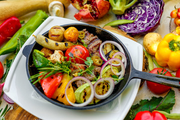 fried meat on the frying pan with vegetables and baked potatoes with vegetables