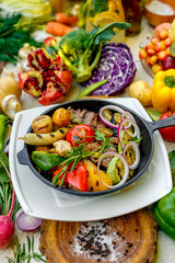 fried meat on the frying pan with vegetables and baked potatoes with vegetables