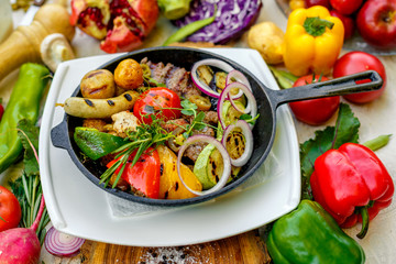 fried meat on the frying pan with vegetables and baked potatoes with vegetables