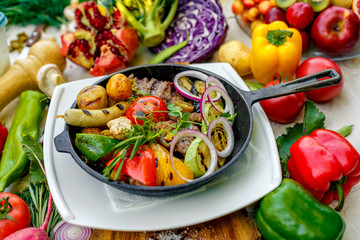 fried meat on the frying pan with vegetables and baked potatoes with vegetables
