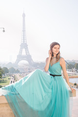 Beautiful girl in an azure evening dress in Paris with the Eiffel tower in the background.