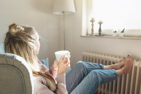 Junge Frau schaut aus dem Fenster und trinkt Tee