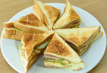 Closeup of ham, egg and vegetable sandwich on the white chopping board.