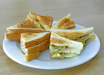 Closeup of ham, egg and vegetable sandwich on the white chopping board.
