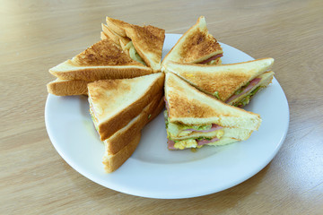 Closeup of ham, egg and vegetable sandwich on the white chopping board.