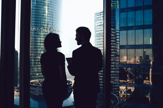 Back View Of Male And Female Colleagues Standing Near Panoramic Window In Enterprise Firm And Discussing Productivity Of Employees, Silhouette Of Successful Corporate Directors Communicate In Office